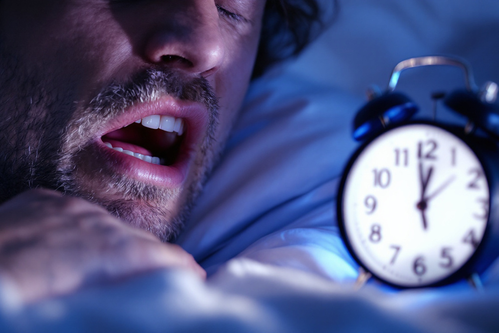 hombre intentando dormir con un reloj despertador iluminado en la noche